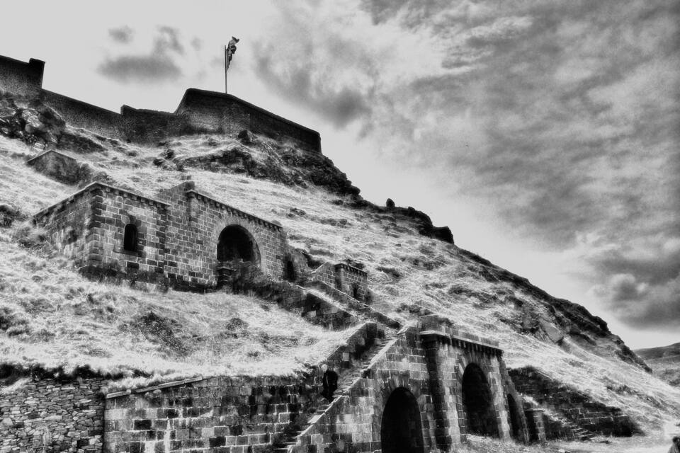 A historical stone structure with arched doorways and a flagpole on a hill.