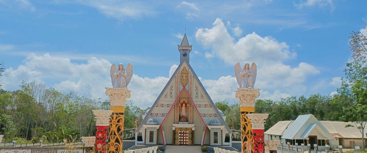 A church with a pointed steeple and two statues of angels on pillars.