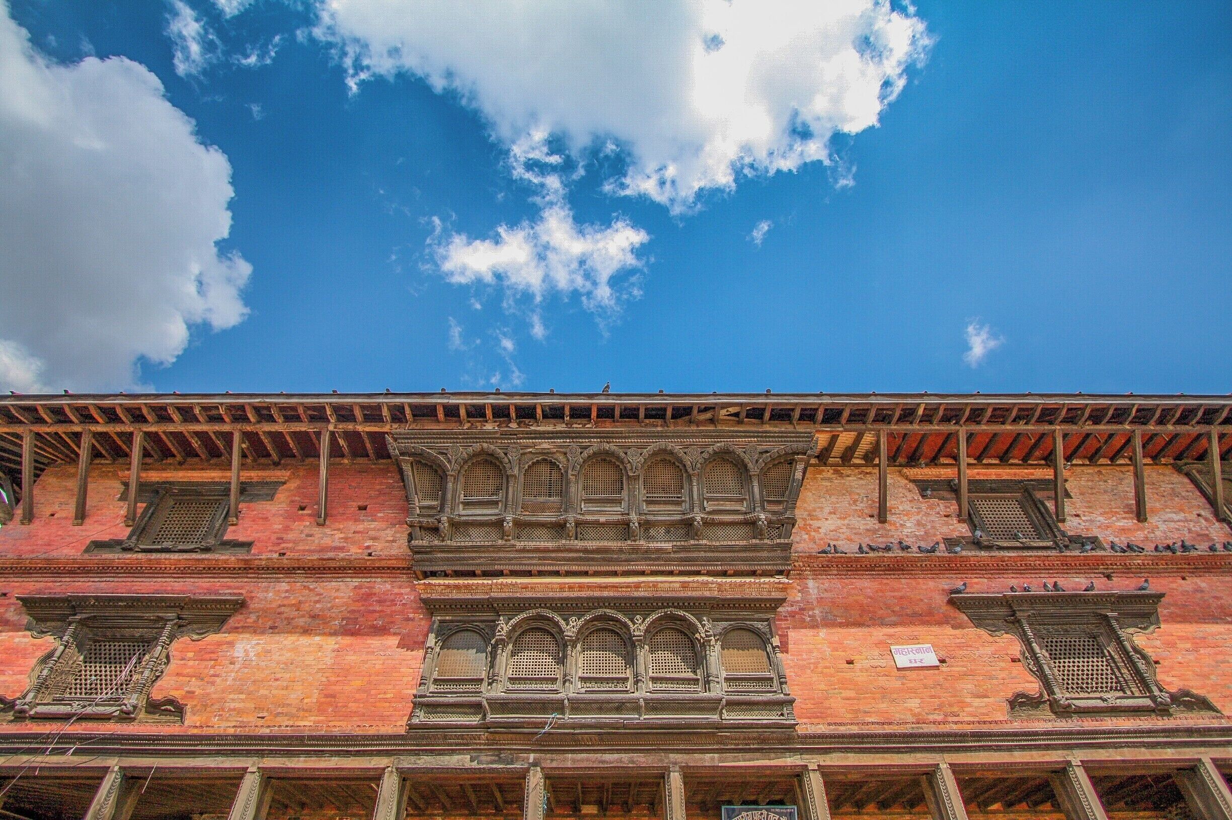 A historic building with ornate windows and a red brick facade under a blue sky with clouds.