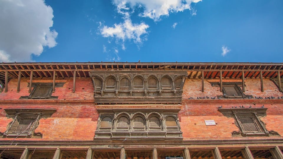 A historic building with ornate windows and a red brick facade under a blue sky with clouds.