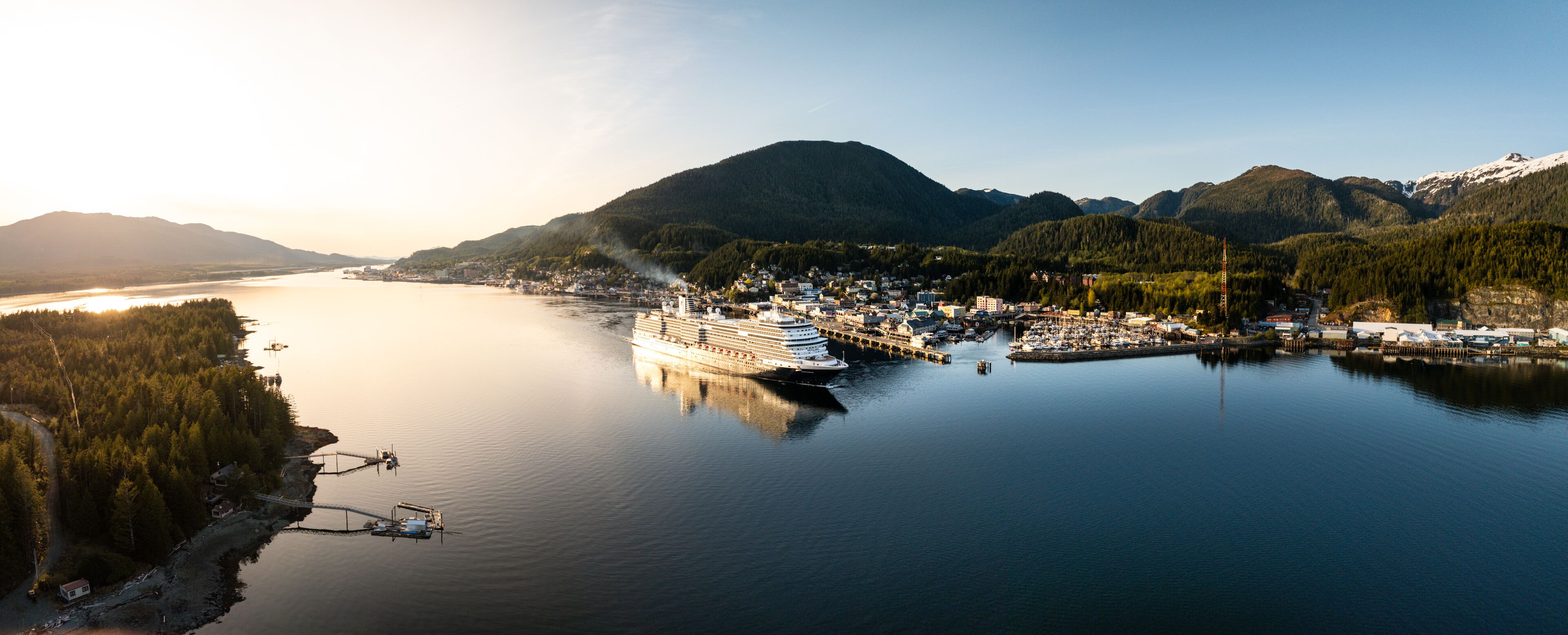 A cruise ship docked at a port surrounded by mountains and a forested coastline.
