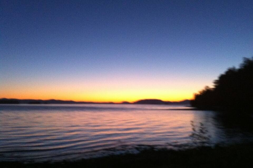 A sunset over a calm body of water with a silhouette of a landmass in the distance.