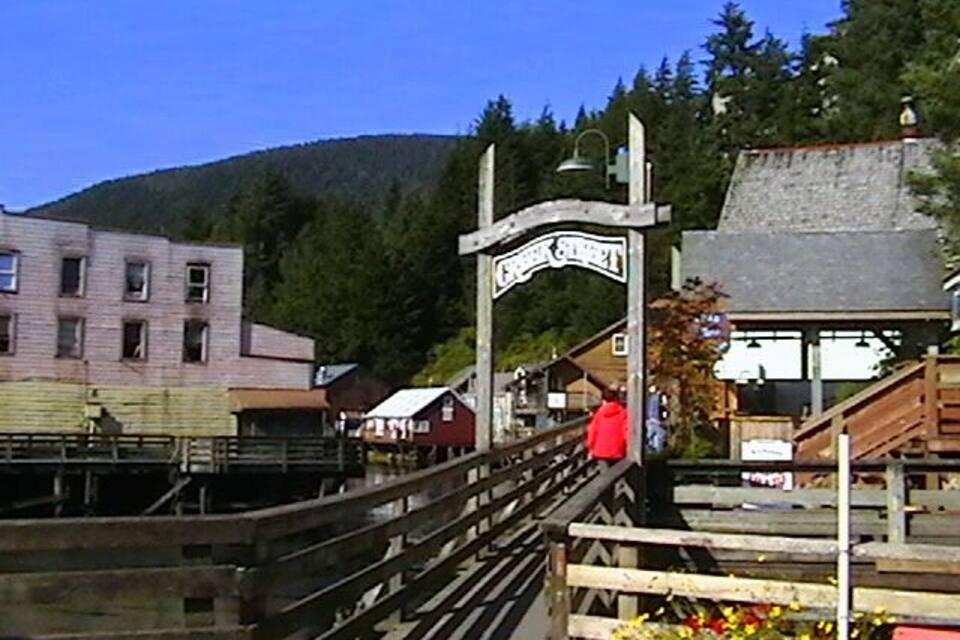 A wooden bridge with a sign, a building with a red roof, and a mountain in the background.