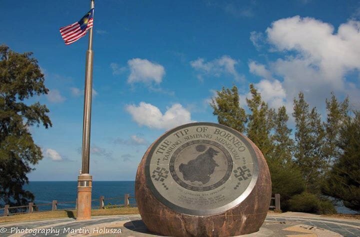 Un monumento con una bandera estadounidense, rodeado de árboles y un cielo despejado.