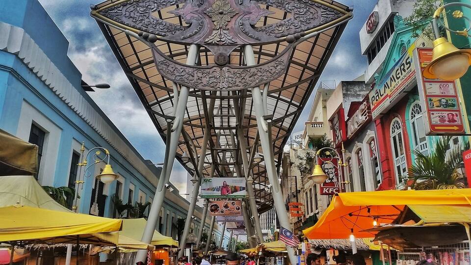 A market street with a central structure featuring intricate metalwork and multiple signs for businesses like KFC and KFC.