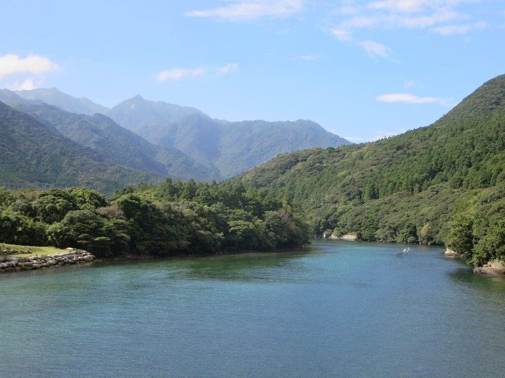 A calm river surrounded by lush green hills and mountains.