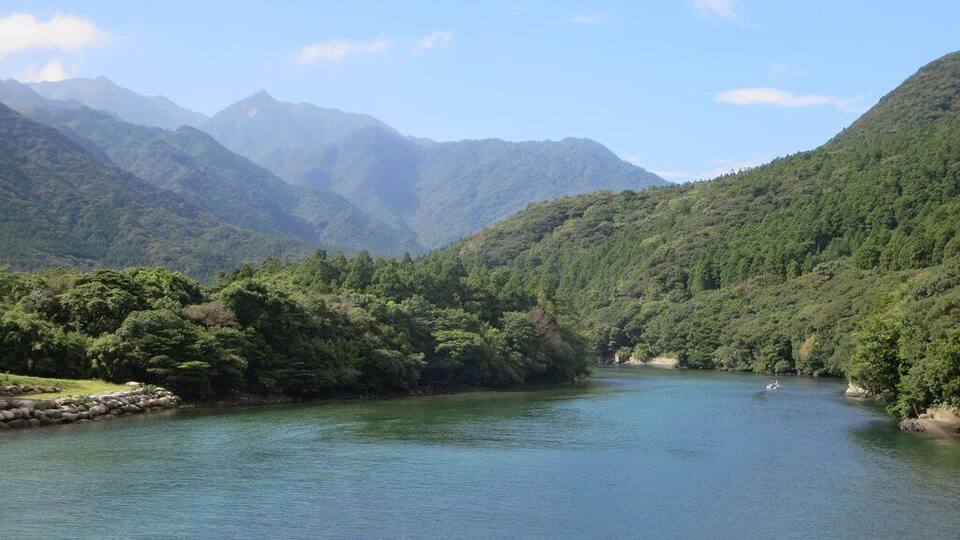 A calm river surrounded by lush green hills and mountains.