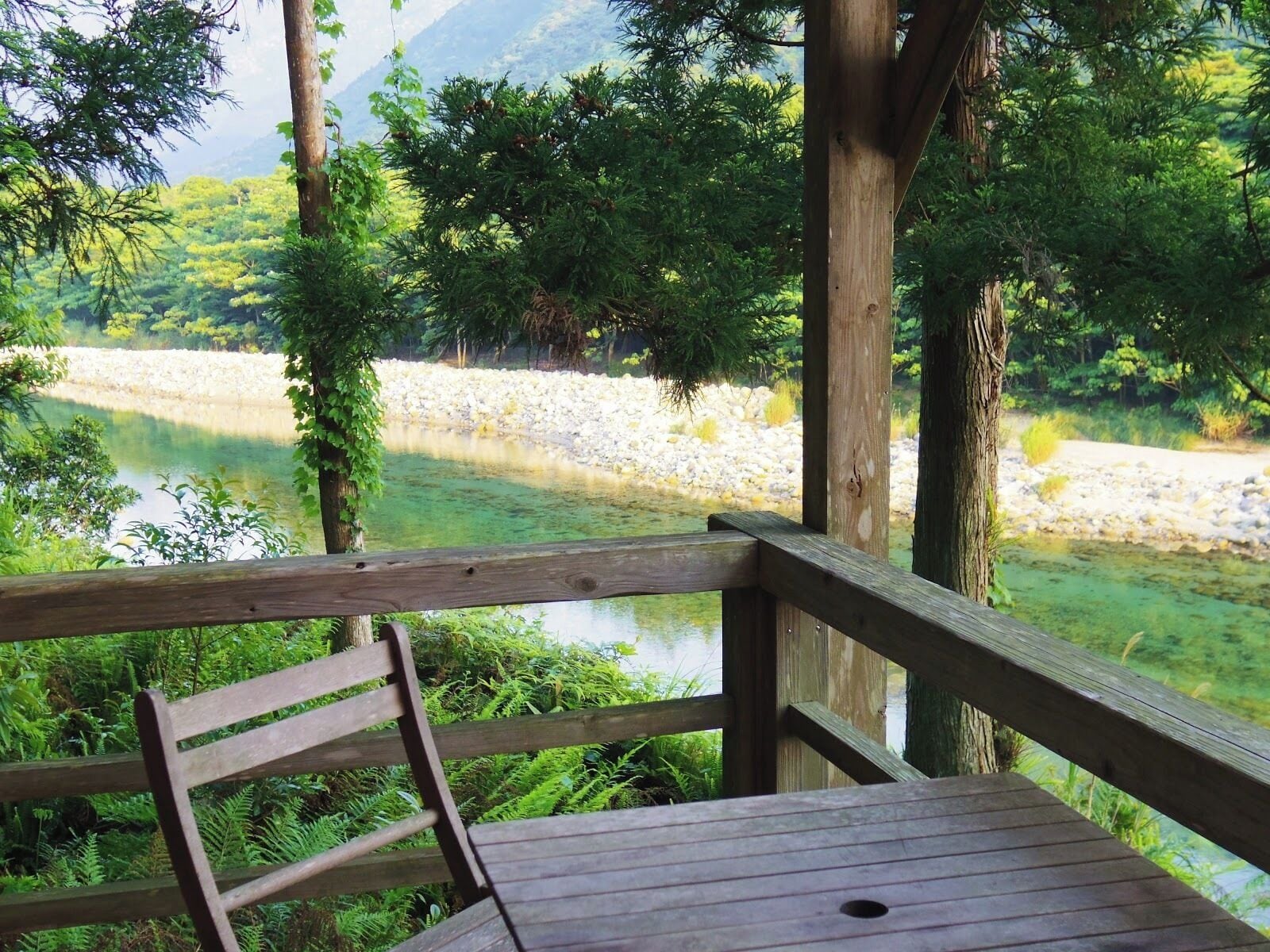 A wooden deck overlooking a river with a rocky riverbank and dense greenery in the background.