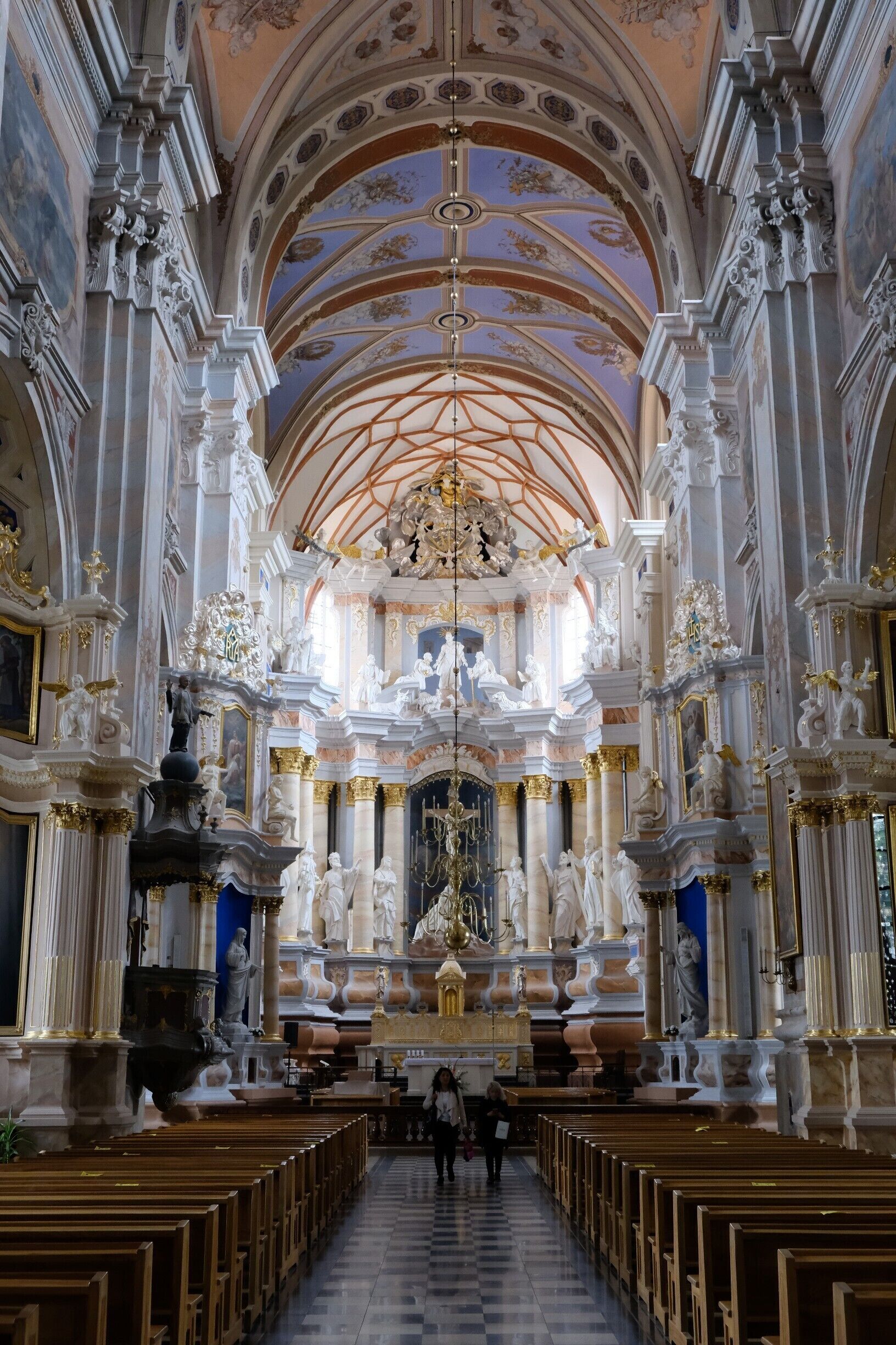 Interior ornamentado de una iglesia con techos altos, esculturas detalladas y filas de bancas.