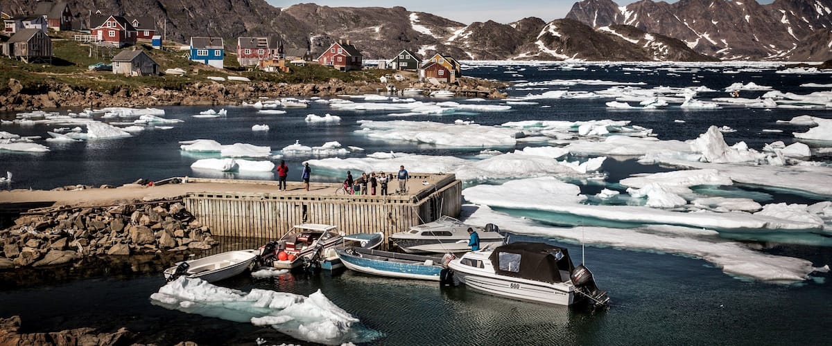 A coastal village with houses, a dock with boats, and icebergs in the water.