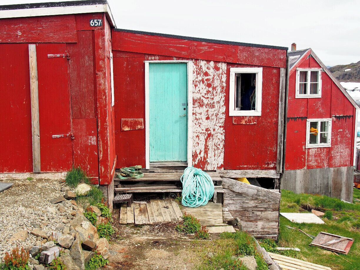Un edificio de madera roja con una puerta turquesa, una ventana pequeña y el número 657 en el costado.