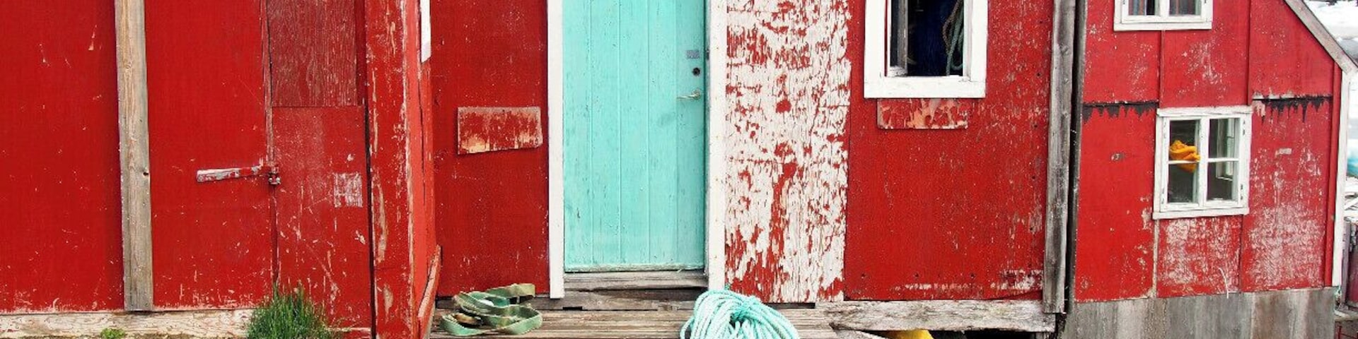 Un edificio de madera roja con una puerta turquesa, una ventana pequeña y el número 657 en el costado.