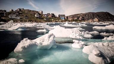 Icebergs en un fiordo con casas en una ladera.