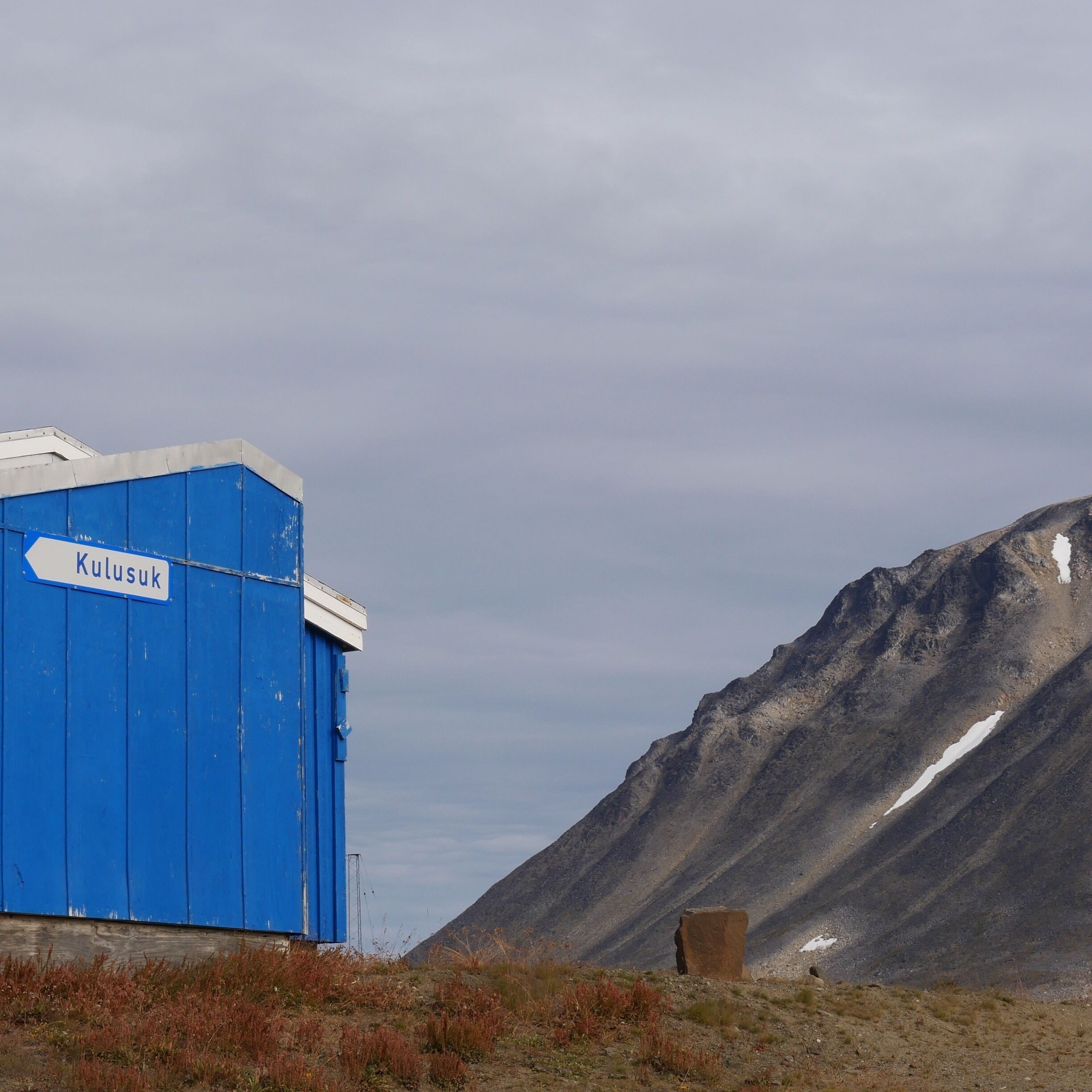 A blue building with a sign reading "Kulusuk" and a mountainous landscape in the background.