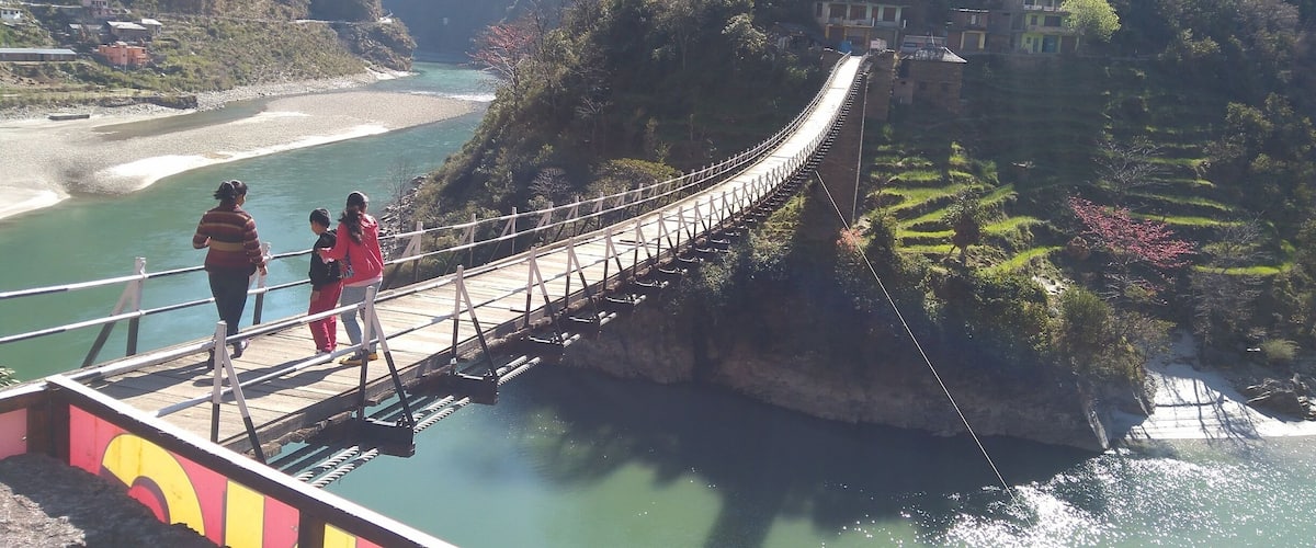 A suspension bridge over a river with terraced fields and houses on the hillside.