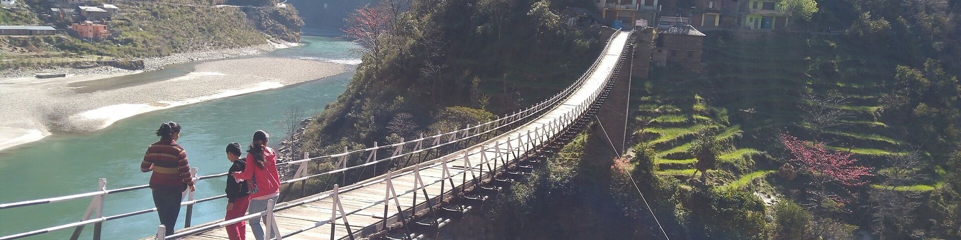 A suspension bridge over a river with terraced fields and houses on the hillside.