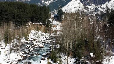A snow-covered river flowing through a mountainous landscape with clear skies.