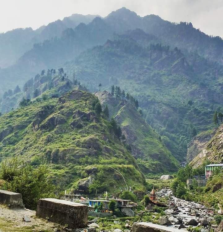 A mountainous landscape with a river, rocky terrain, and a small building.