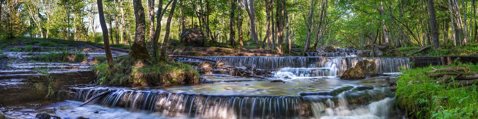Silverfallet Staircase Waterfall illuminated by low rays of the sun in Lush serene forest and rural mill environment near town Skovde, Sweden