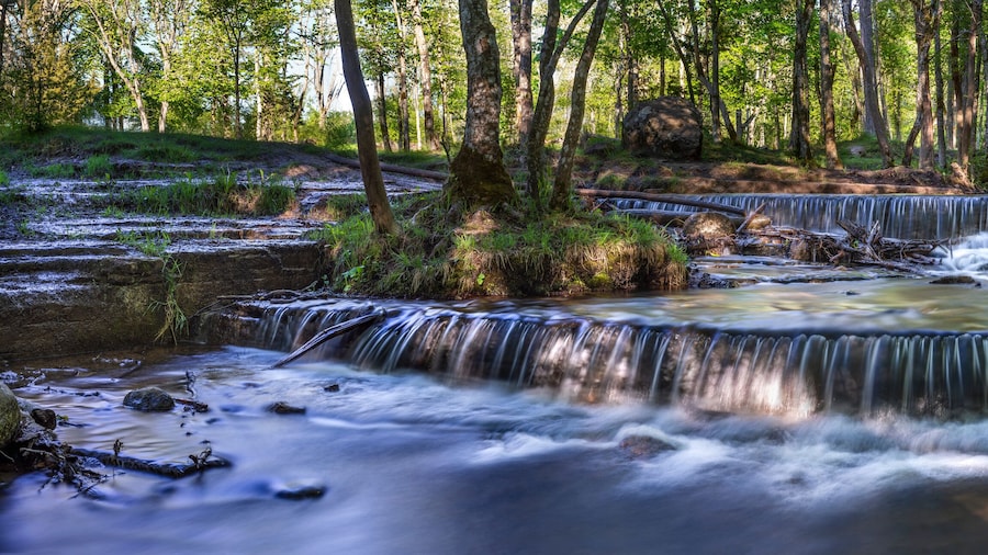 Silverfallet Staircase Waterfall illuminated by low rays of the sun in Lush serene forest and rural mill environment near town Skovde, Sweden
