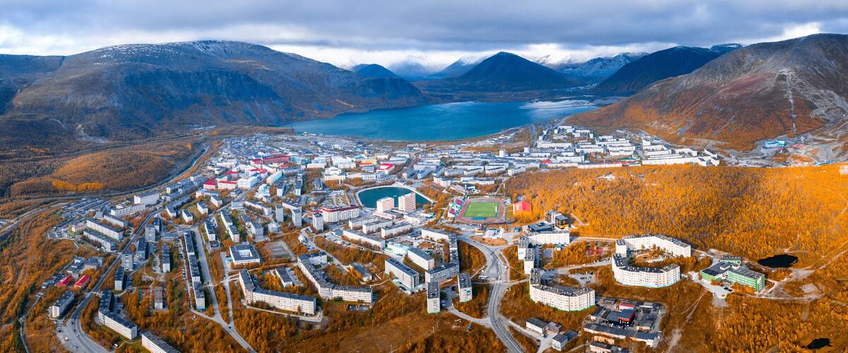 An aerial view of a town with a lake, surrounded by mountains and autumn-colored trees.