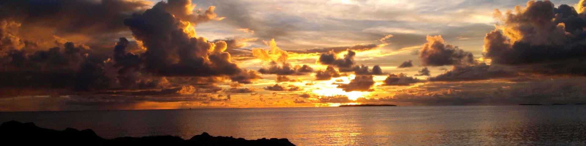 Ein Sonnenuntergang über einem ruhigen Meer mit verschwommenen Landzügen im Vordergrund und vereinzelten Wolken.