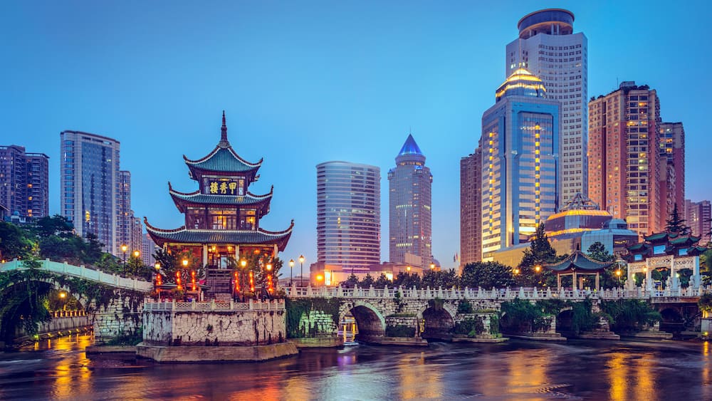 A traditional Chinese pagoda by a river with modern skyscrapers in the background.