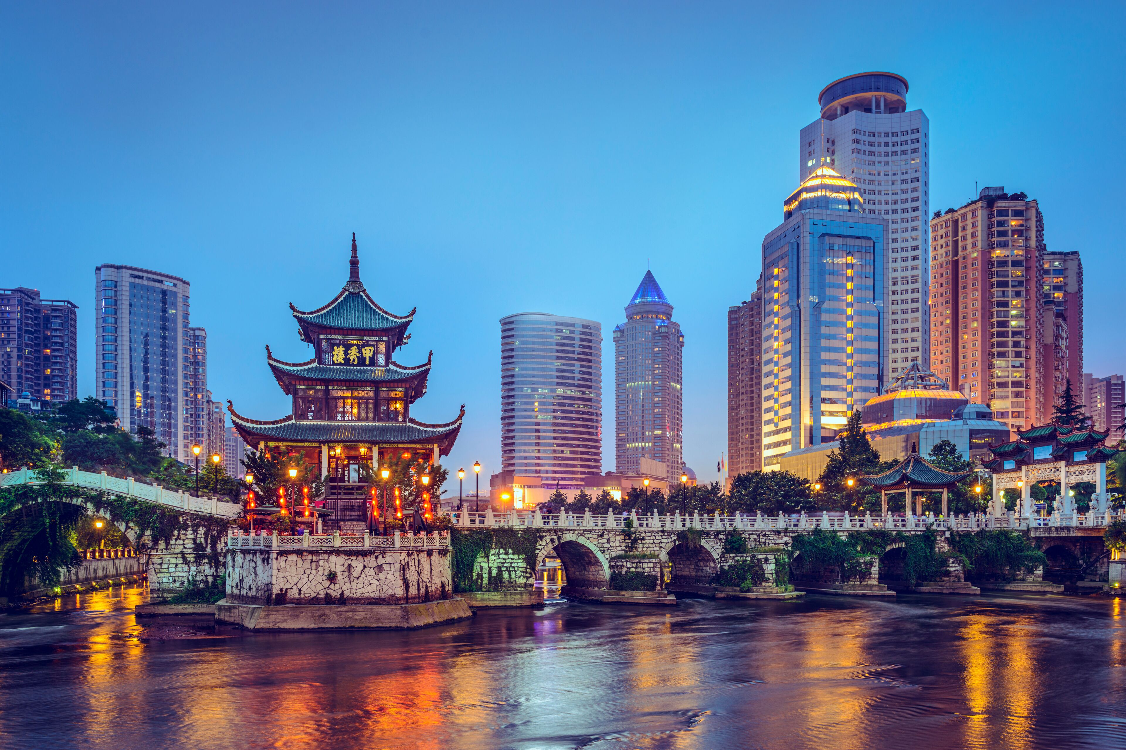 A traditional Chinese pagoda by a river with modern skyscrapers in the background.