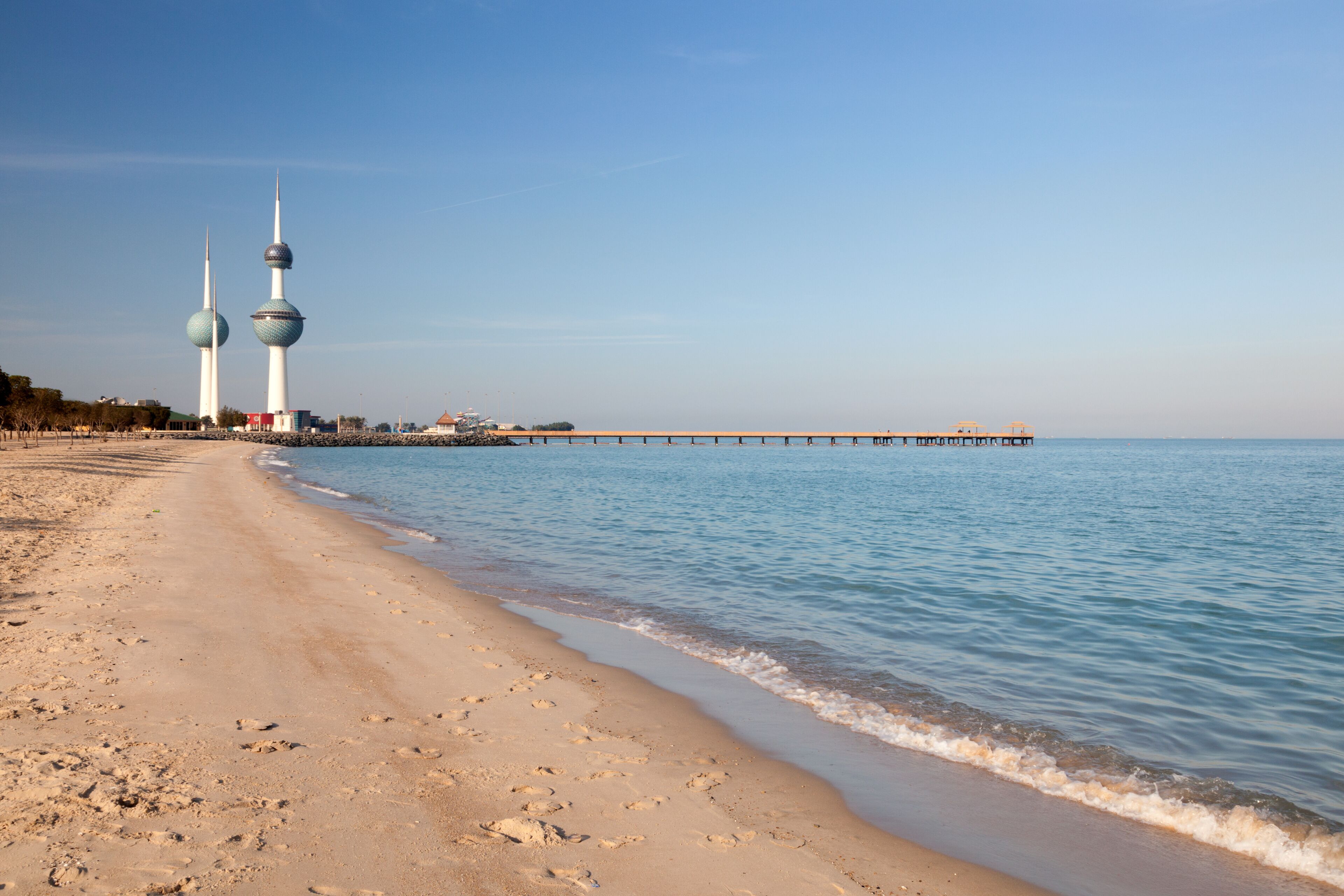 Ein Strand mit Fußabdrücken, ruhigem Wasser und zwei Türmen im Hintergrund.