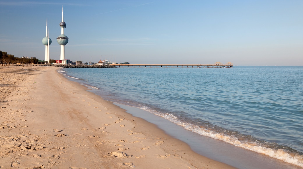 Ein Strand mit Fußabdrücken, ruhigem Wasser und zwei Türmen im Hintergrund.