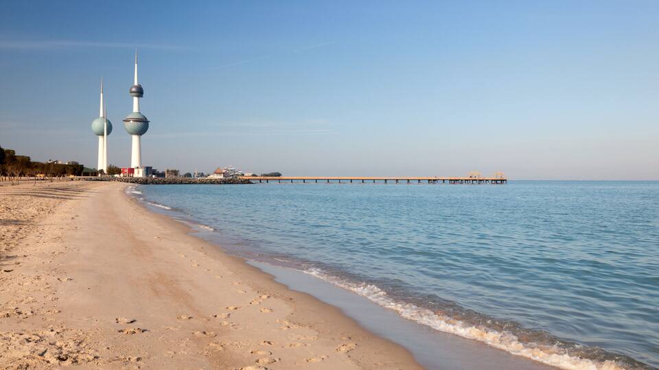 A beach with footprints, calm water, and two prominent towers in the background.