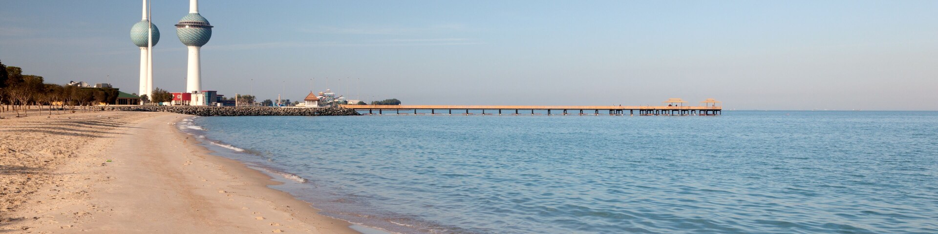 Una playa con huellas, agua tranquila y dos torres destacadas al fondo.