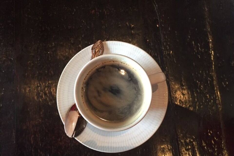 A cup of coffee on a saucer on a wooden table.