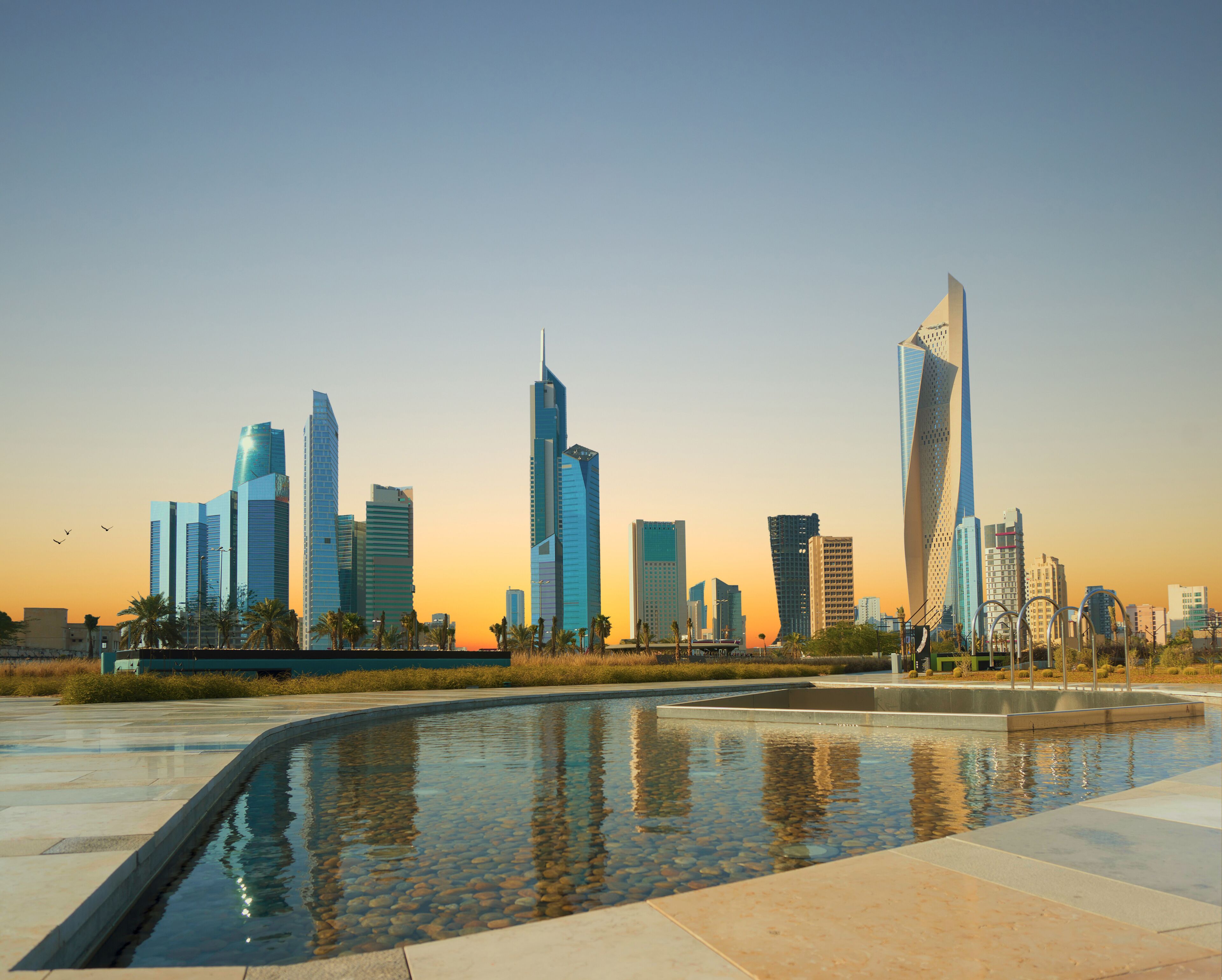 A city skyline with modern skyscrapers and a reflective water feature.