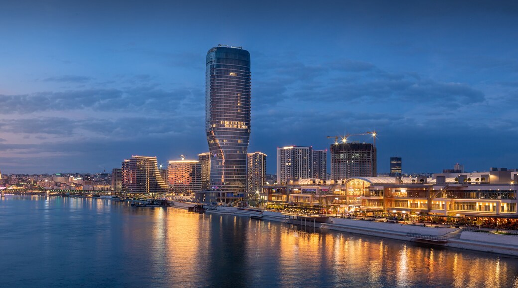 A city skyline with a prominent curved skyscraper, a river reflecting lights, and a bridge in the background.