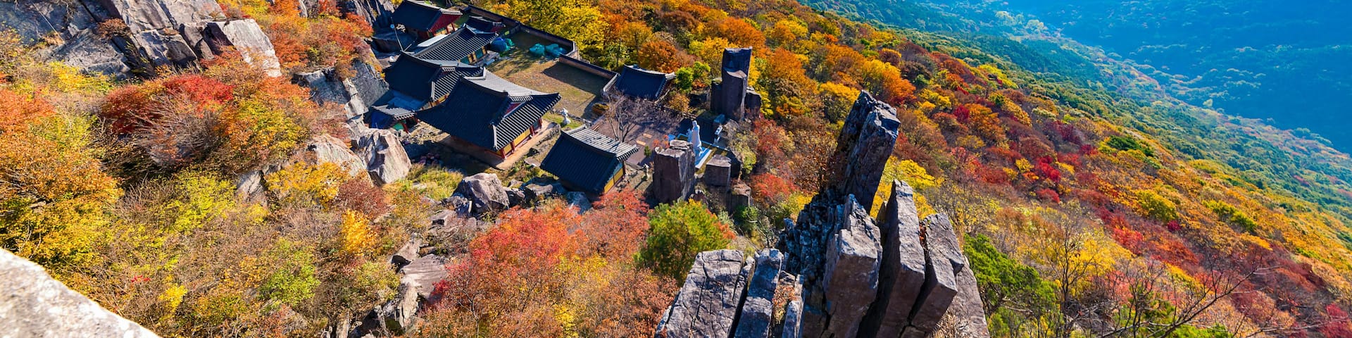 A mountainous landscape with traditional Korean architecture amidst autumn foliage.
