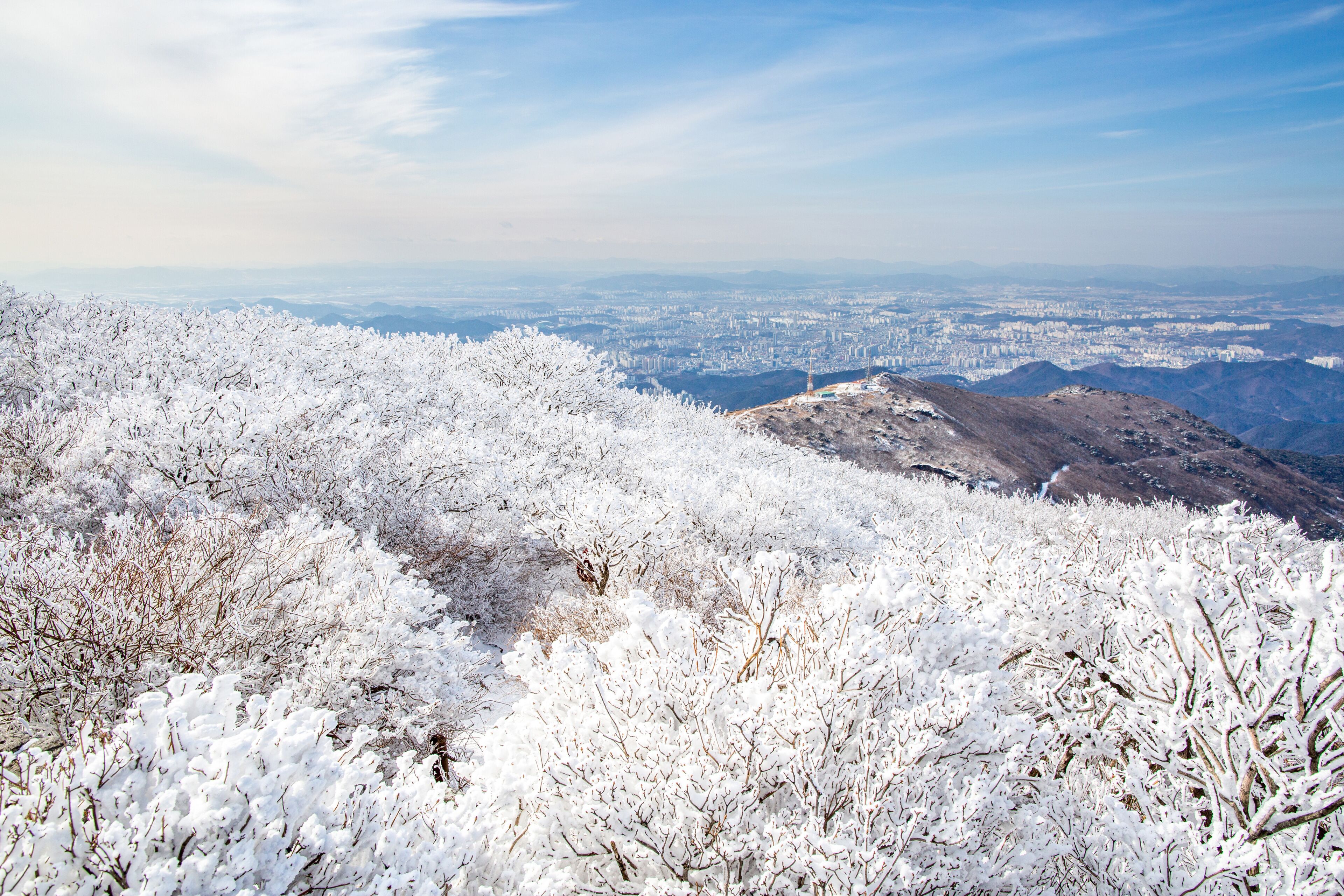 Aerial and winter view of hoarfrost on the tree and ridge of Mudeungsan Mountain with the background of downtown Gwangju, South Korea 