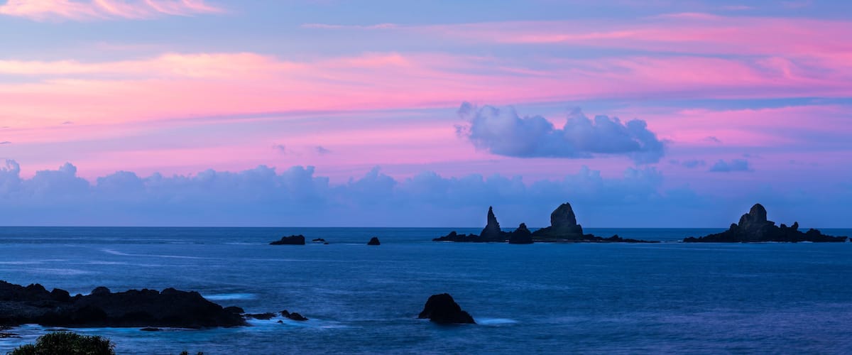A coastal landscape with rocky outcrops and a colorful sky.