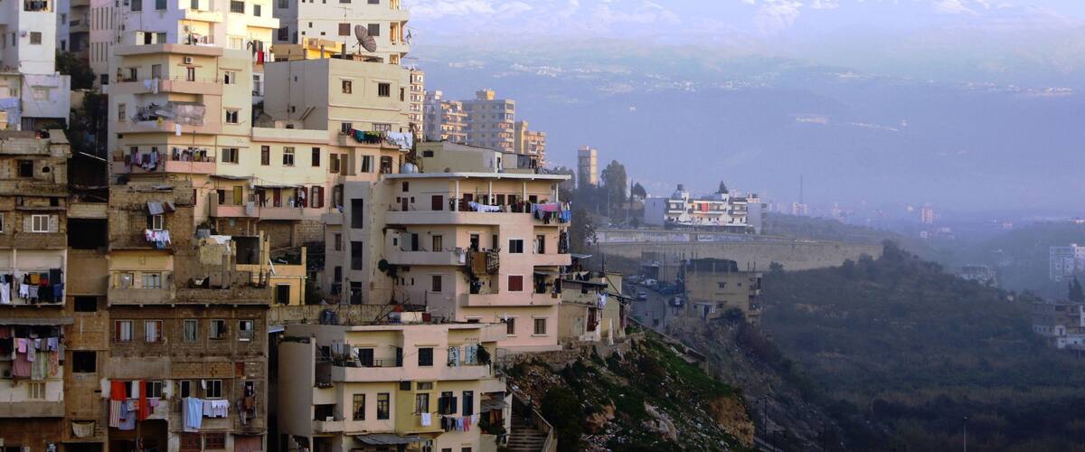 A densely packed hillside of multi-story buildings with visible balconies and laundry hanging out to dry, overlooking a distant cityscape and mountains.