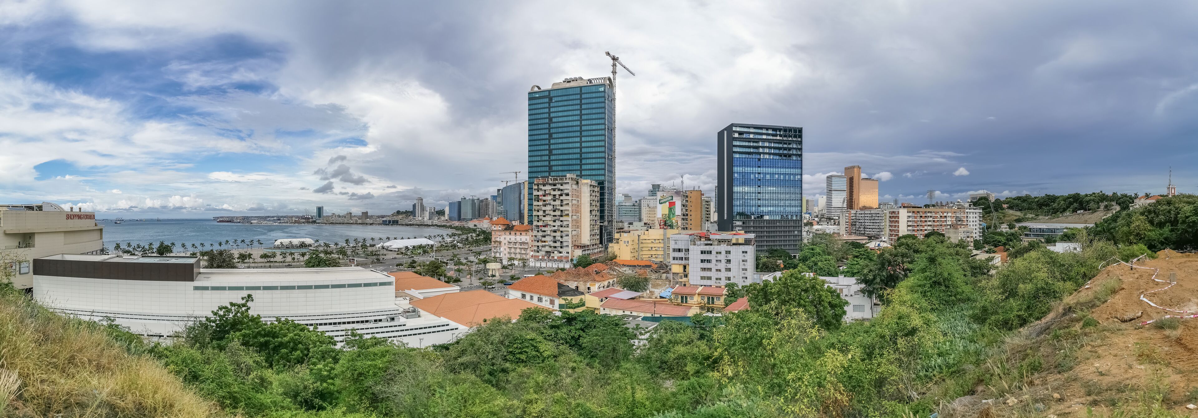 A coastal cityscape with modern skyscrapers, a beach, and lush greenery.