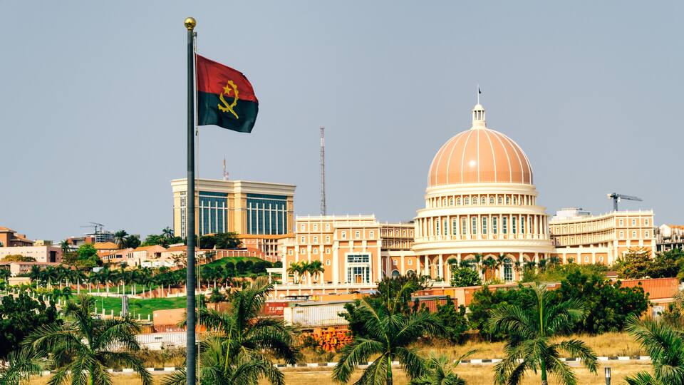 A large building with a dome, palm trees, and a flag.