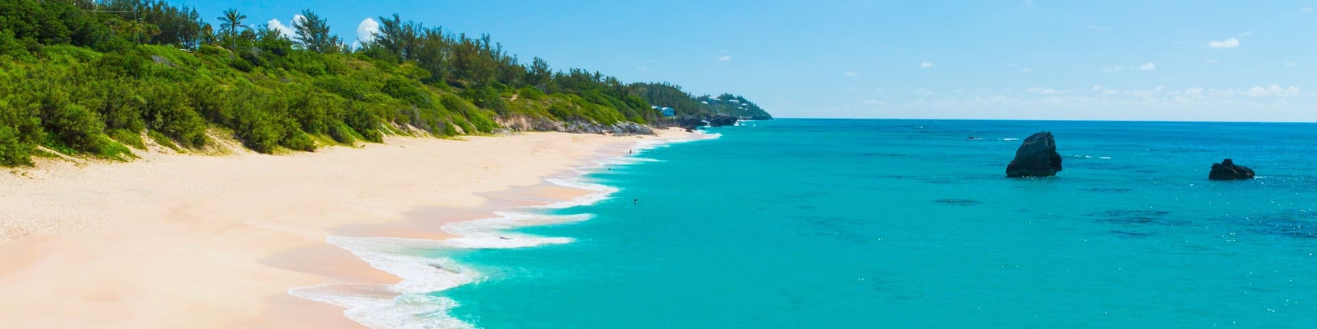 A beach with clear turquoise water, sandy shore, and lush greenery.
