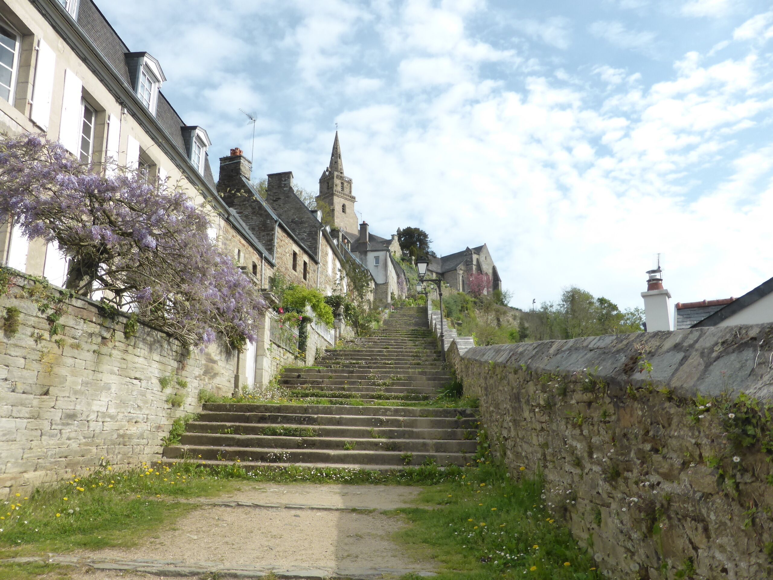 A stone staircase leading up to a church with a spire, surrounded by flowering trees and historic buildings.