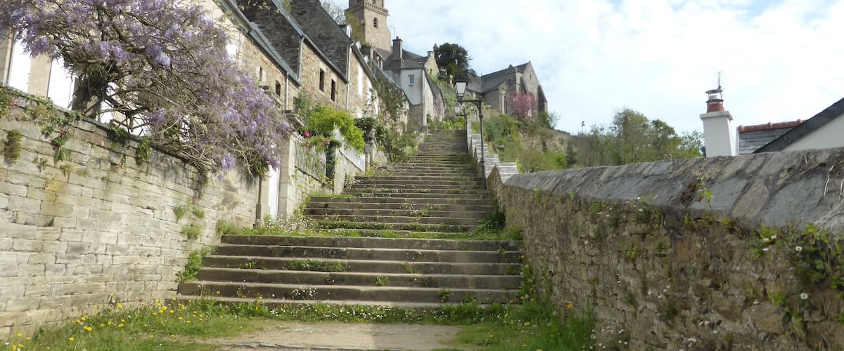 A stone staircase leading up to a church with a spire, surrounded by flowering trees and historic buildings.