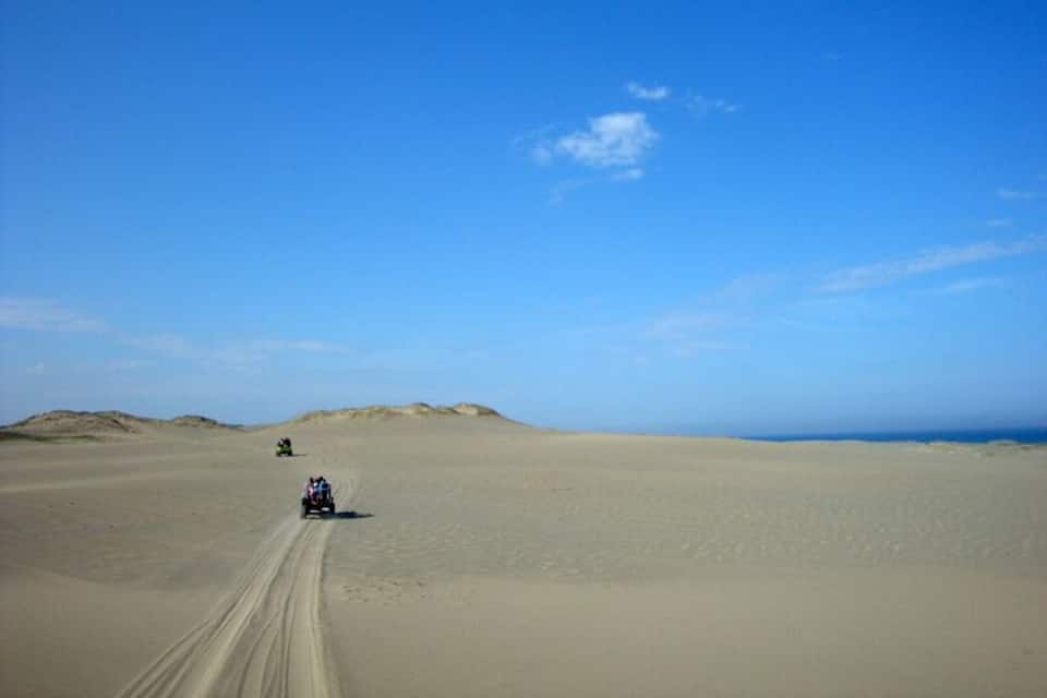 A desert landscape with sand dunes and a vehicle driving on the sand.