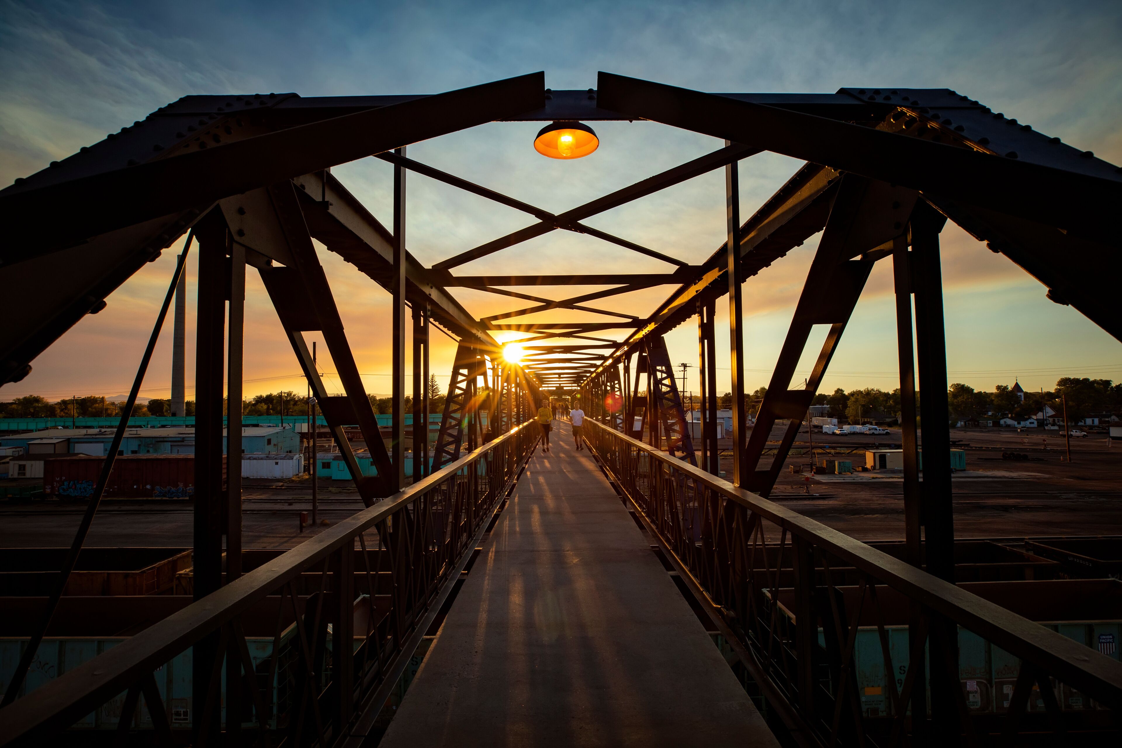 A metal bridge with a walkway, metal beams, and a sunset in the background.