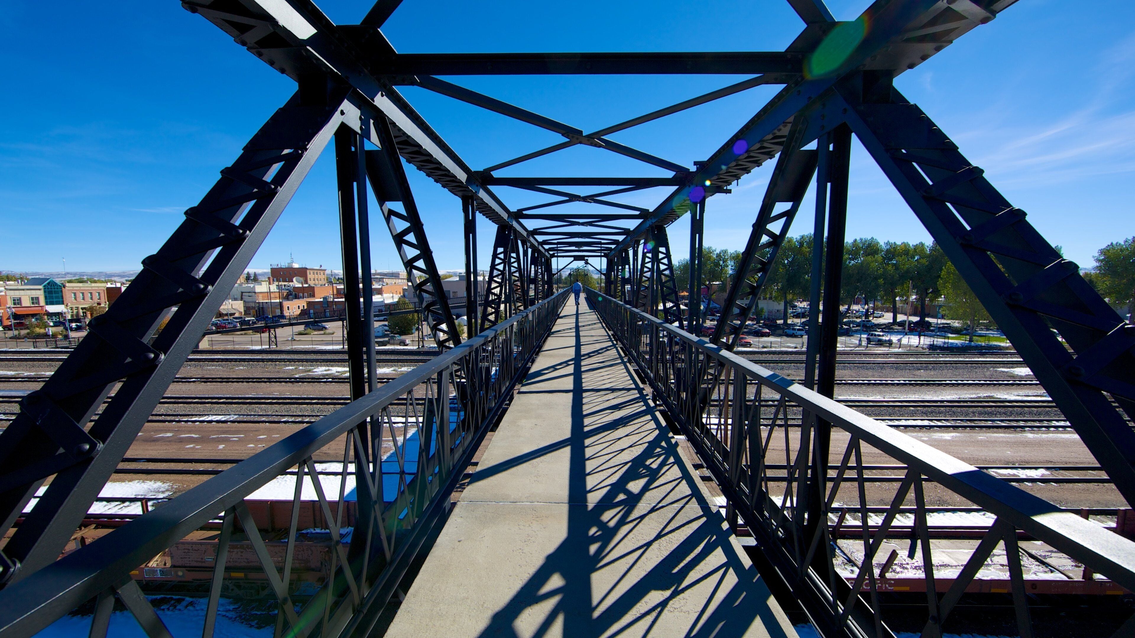 A steel bridge with a clear sky, tracks, and buildings in the background.