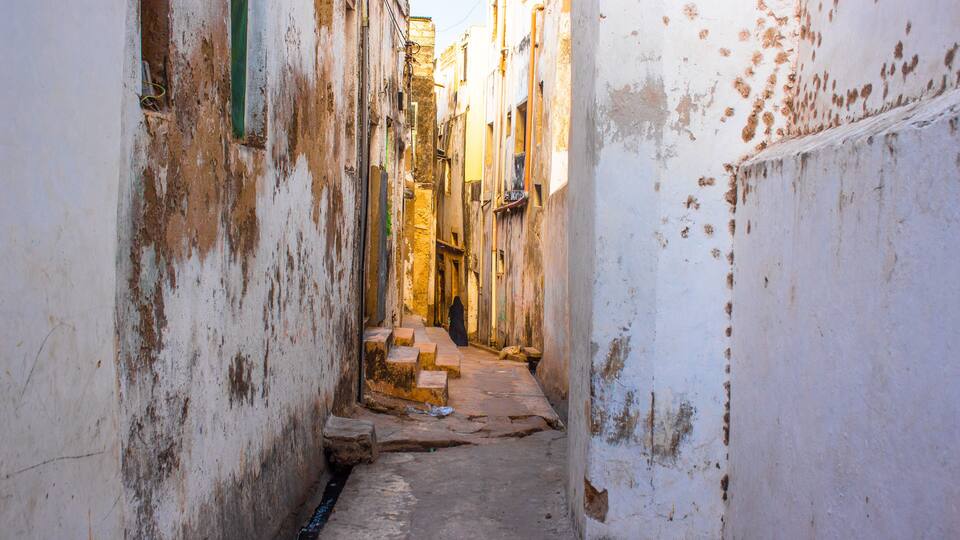 A narrow alley with weathered walls and steps leading to a building.