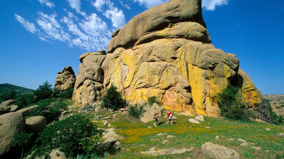 A large rock formation with hikers on a grassy path.