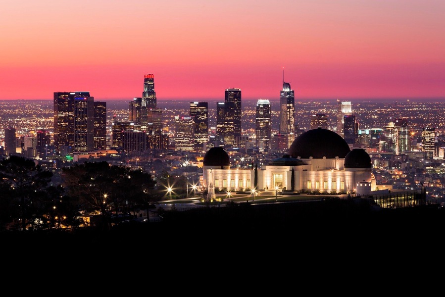 A city skyline at dusk with illuminated buildings and a prominent dome structure in the foreground.
